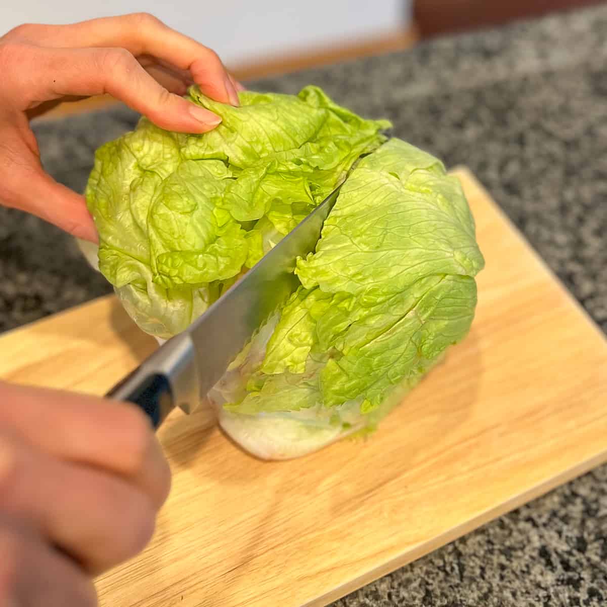 top side view of a head of iceberg lettuce being cut with a knife into a lettuce bun