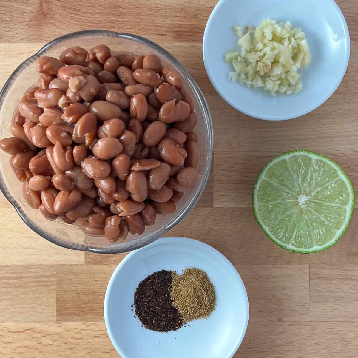 top view of the key ingredients for chipotle pinto beans: pinto beans, minced garlic, chipotle powder, cumin and fresh lime