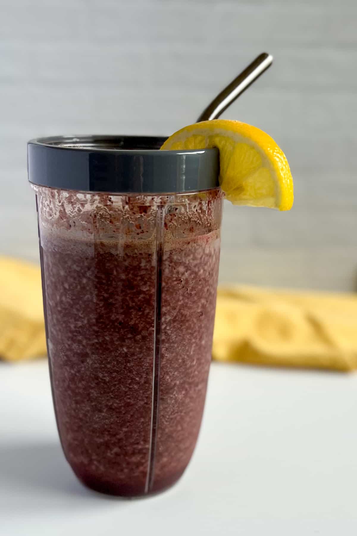 side view close up of icy deep red/purple immunity smoothie in a cup with gray rim and lemon wedge on the rim; metal straw sticking out