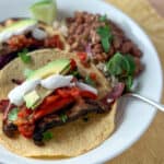 top side view close up of two mushroom fajitas with peppers, onion, avocado and cashew sour cream; beans blurred in the background