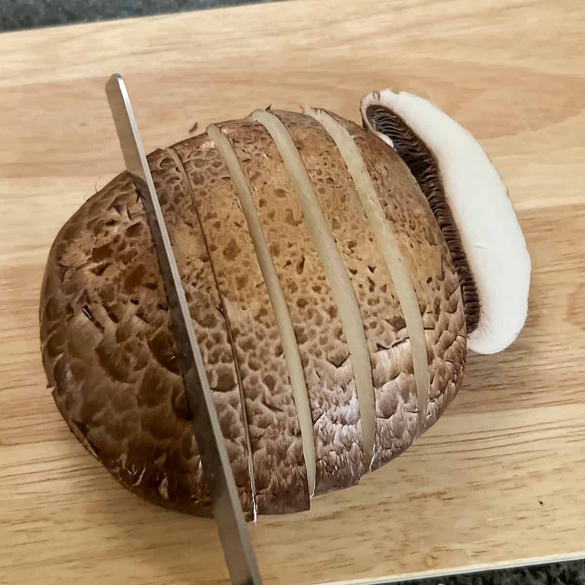 top view of a portobello mushroom being sliced on wooden board