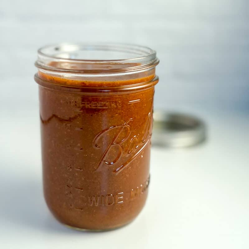 side view close up of red enchilada sauce in a mason jar with lid blurred in the background