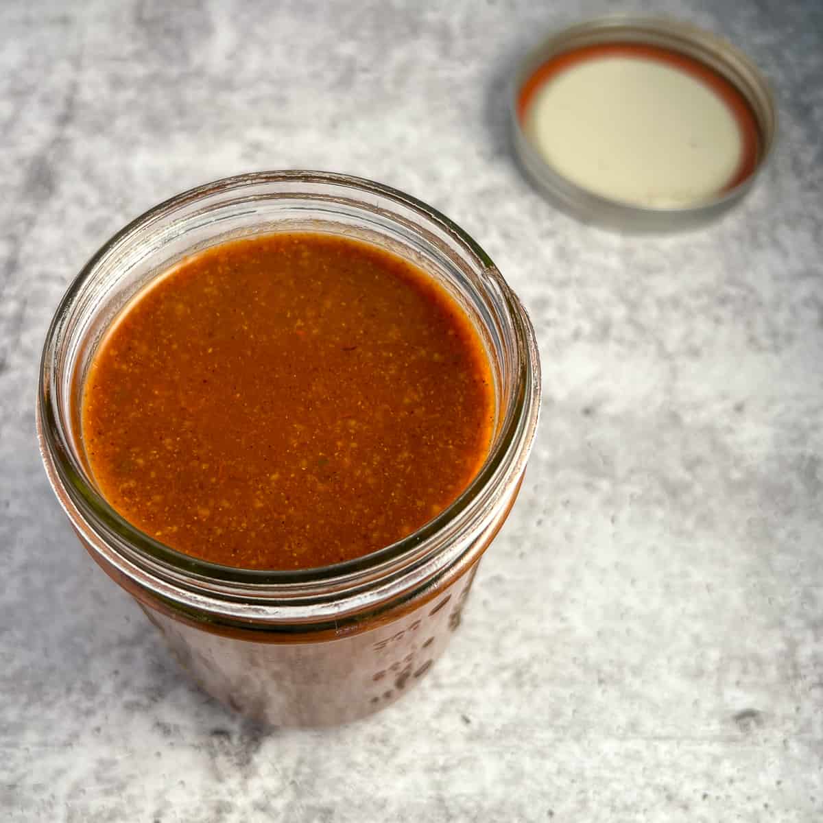 top view close up of red enchilada sauce in a mason jar with lid blurred in the background
