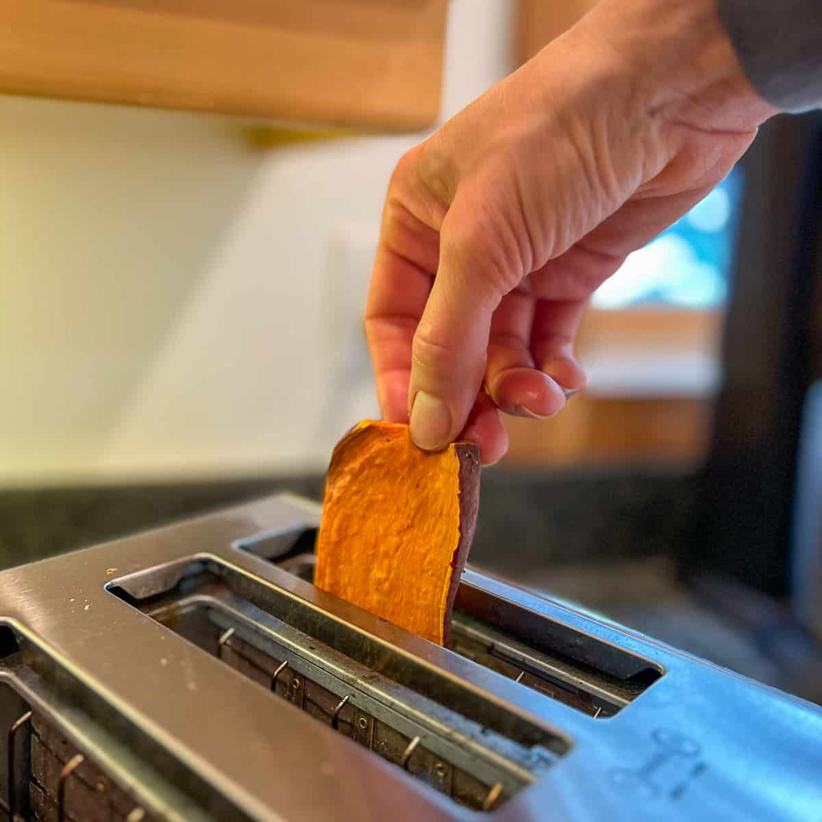 side view of a woman's hand placing a slice of sweet potato toast into the toaster
