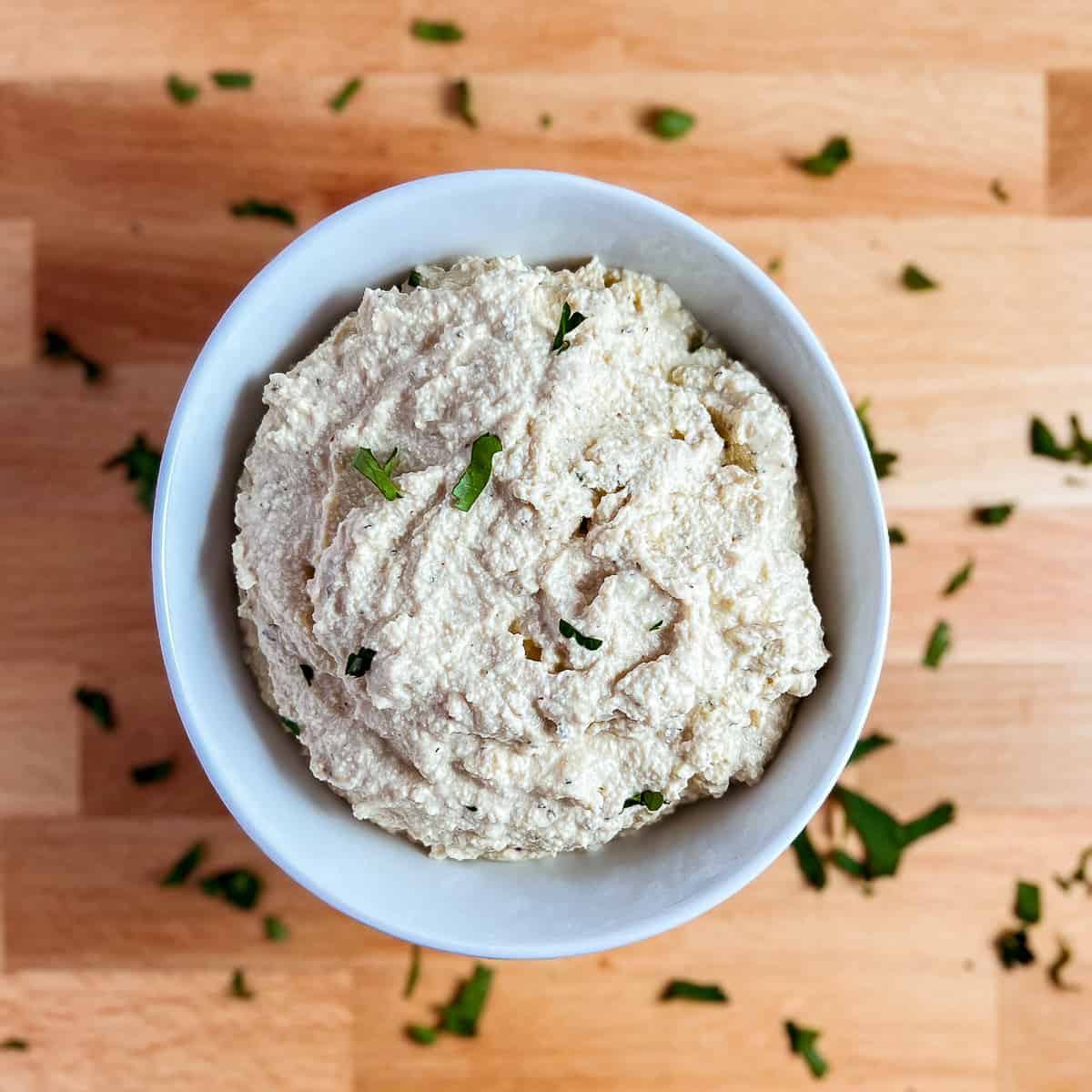 top view close up of vegan tofu ricotta in a round white bowl with finely chopped fresh parsley on top and around the side of the bowl