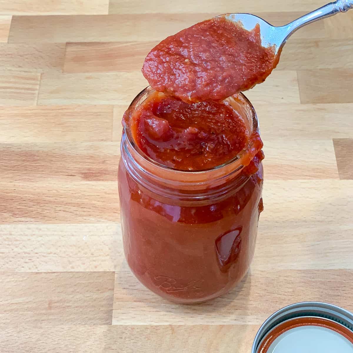 top side close up of vegan bbq sauce in a mason jar with a spoon full of sauce lifted out