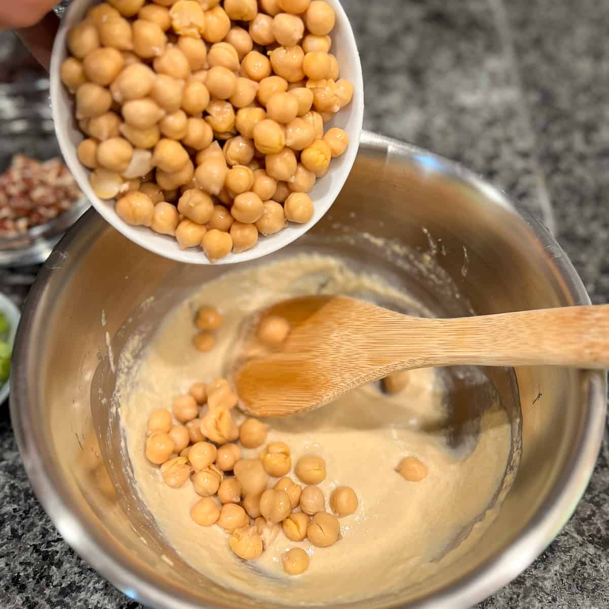 chickpeas being added to the sauce mixture in the stainless mixing bowl