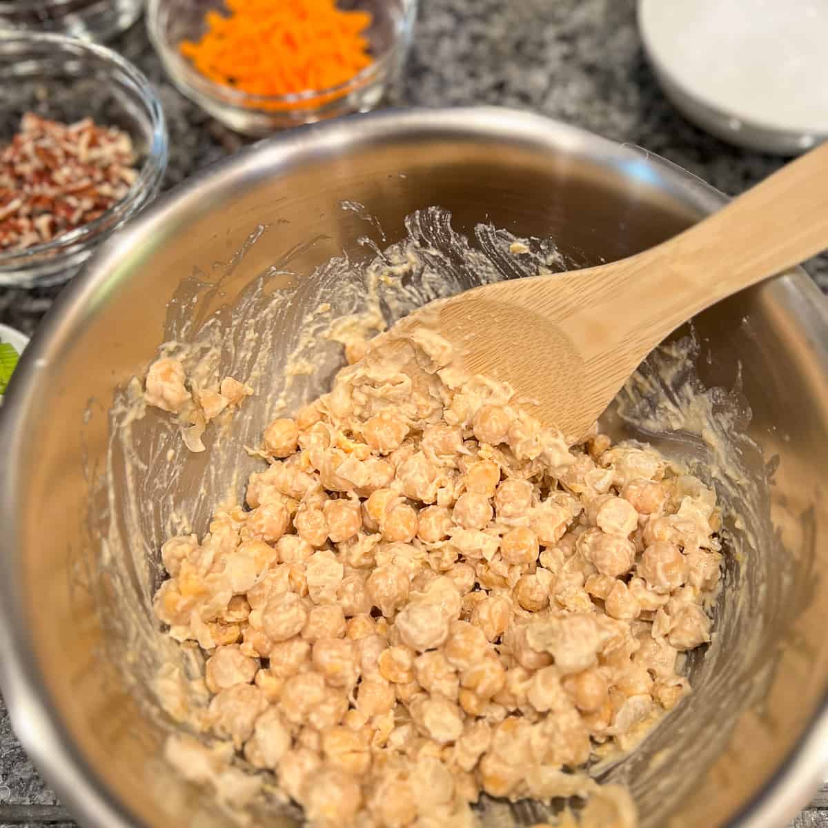 chickpeas mixed into the sauce mixture in mixing bowl with wooden spoon