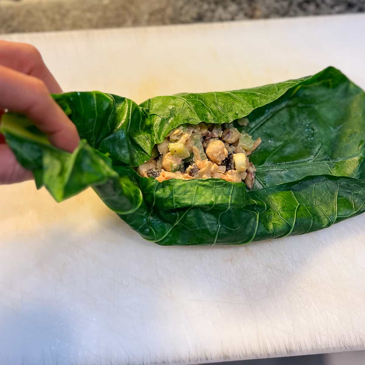woman's hand wrapping the chickpea salad in a collard green leaf