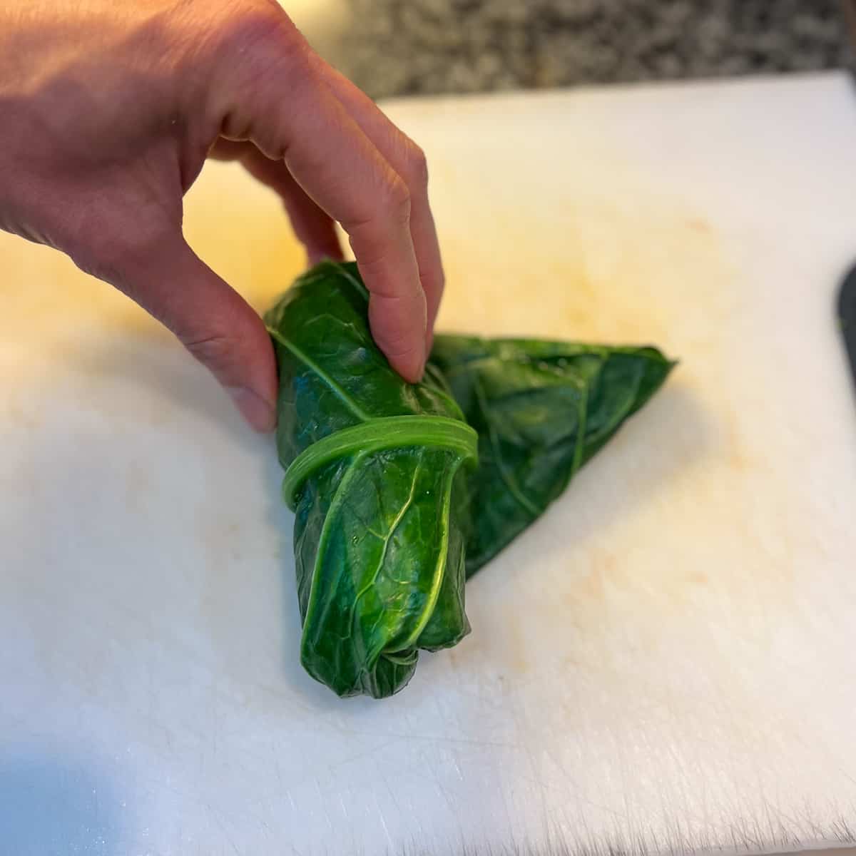 a woman's hand rolling the collard green leaf with chickpea salad mixture into a handheld wrap