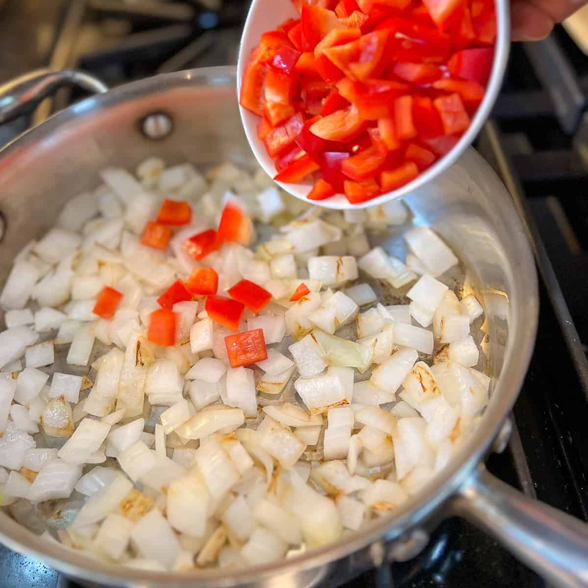 chopped red bell pepper being added to hot pan with onions