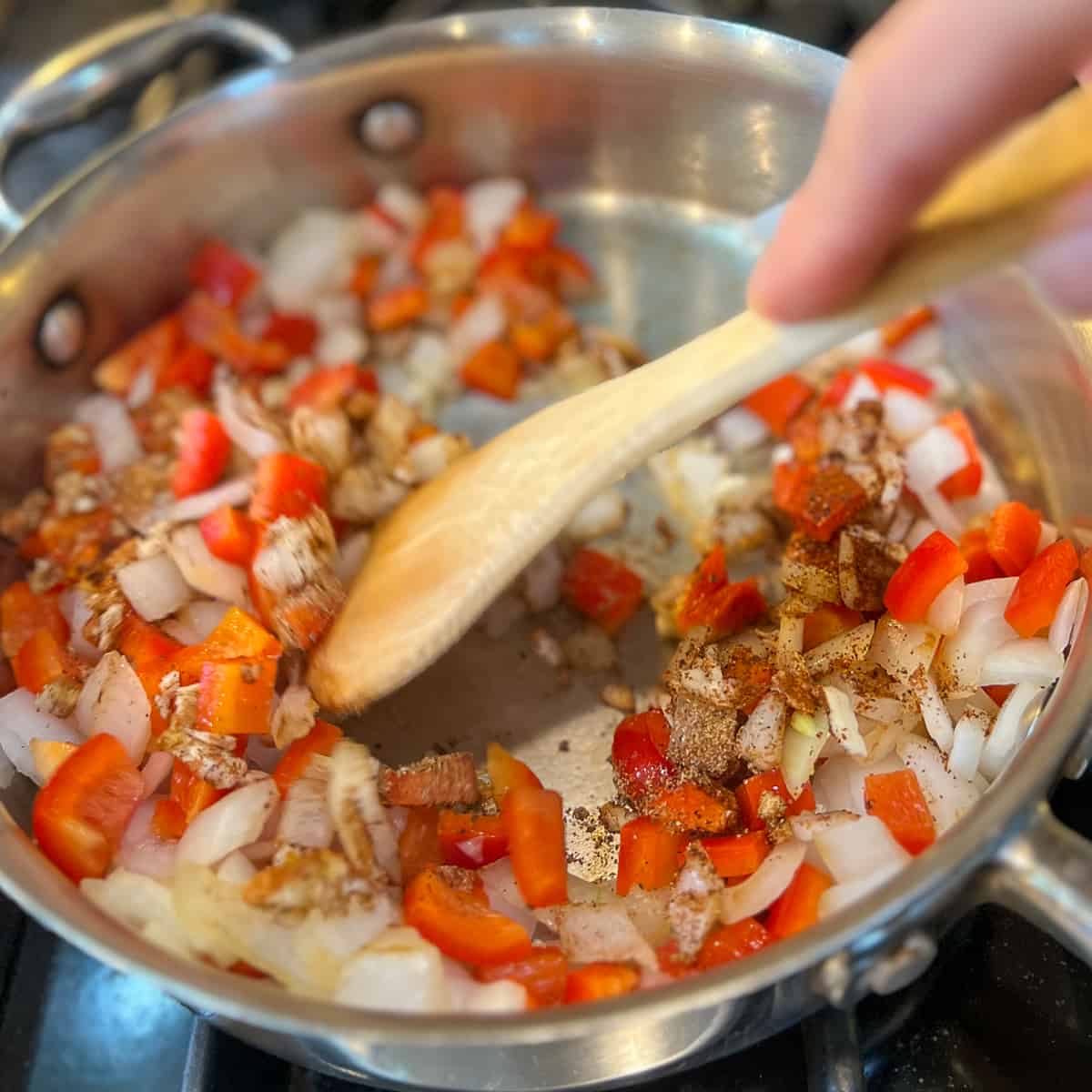wooden spoon stirring veggies and spices in pan on the stovetop