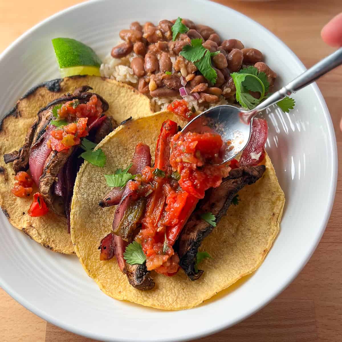 Vegan fajitas on a plate with a spoon adding salsa to the top; side of beans and rice.
