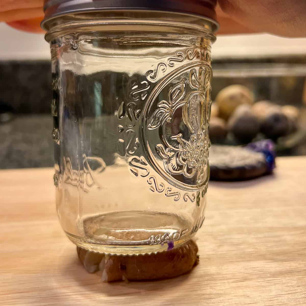 side view of a woman's hand pressing the mason jar over the cooked potato and smashing it. 