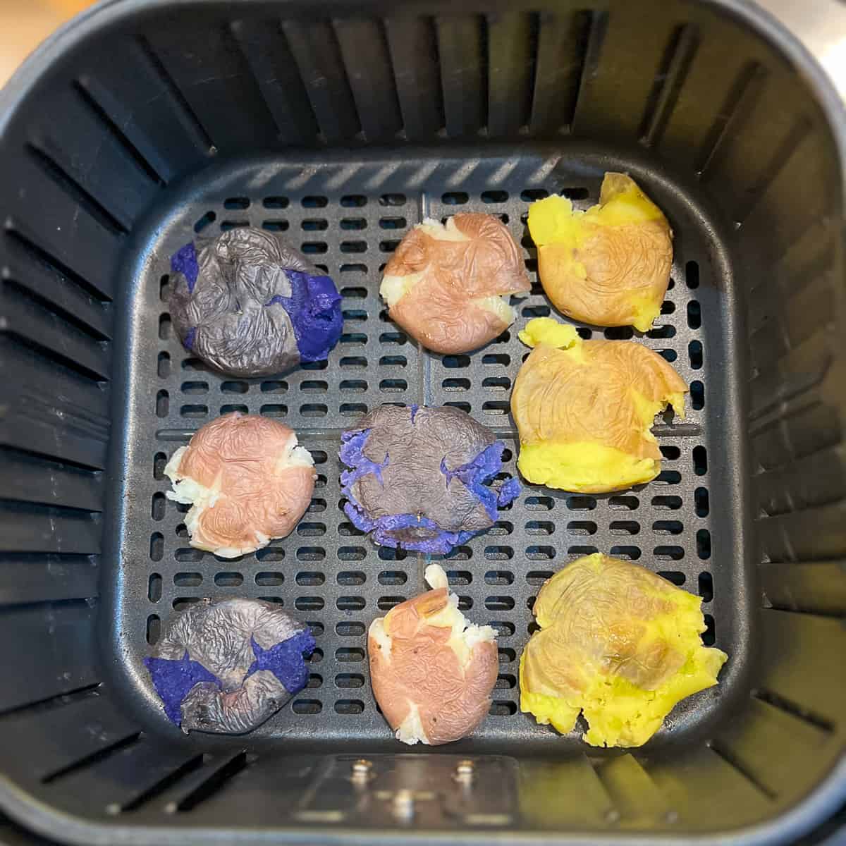top view of nine colorful smashed potatoes in the basket of an air fryer