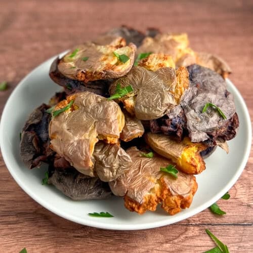 top side view of a pile of petite air fryer smashed potatoes on a white plate topped with fresh chopped parsley and black pepper