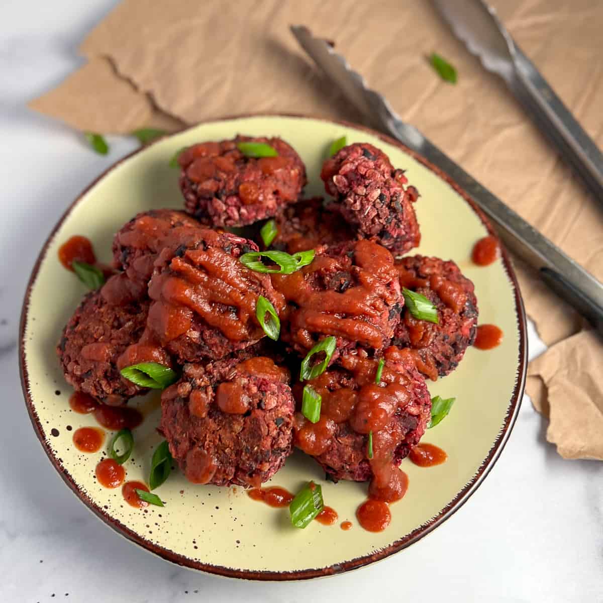 A plate of vegan sliders on a plate topped with barbeque sauce and thinly sliced green onion. 