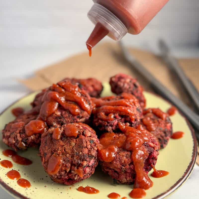 A pile of vegan black bean sliders with bbq sauce being poured on top.