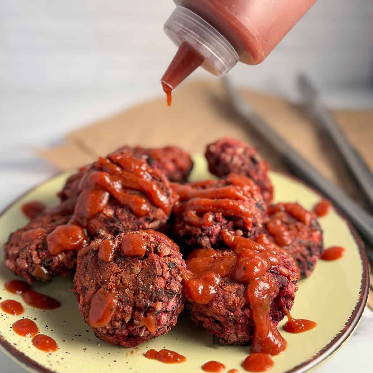 A pile of vegan sliders on a plate drizzled with barbeque sauce.