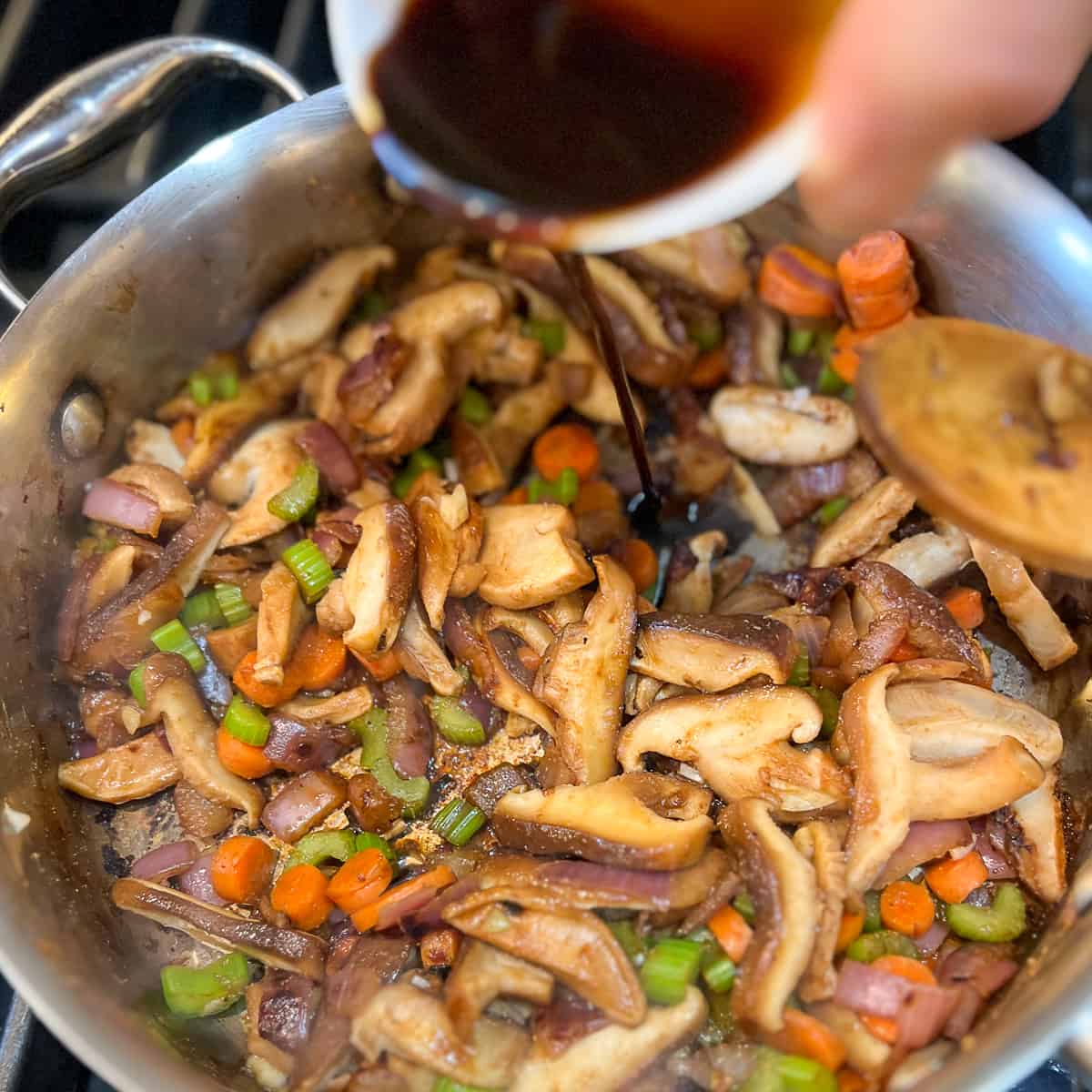 top side view of coconut aminos being added to a sauce pan with cooked mushrooms and veggies