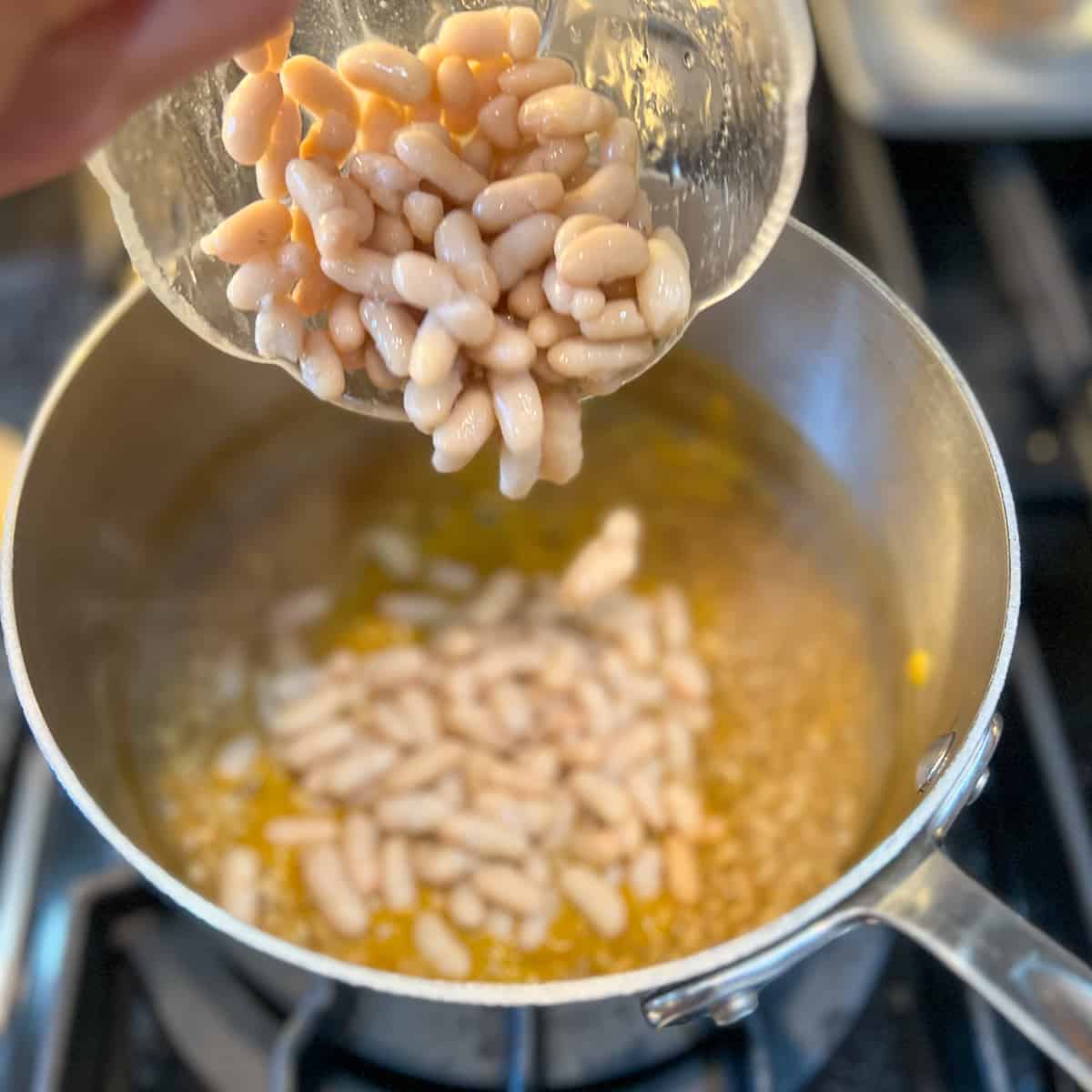 top side view of cooked cannellini beans being added to the pot with barley and veggie broth