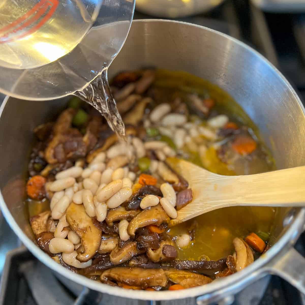 top side view of water being added to the mushroom barley soup pot with cannellini beans