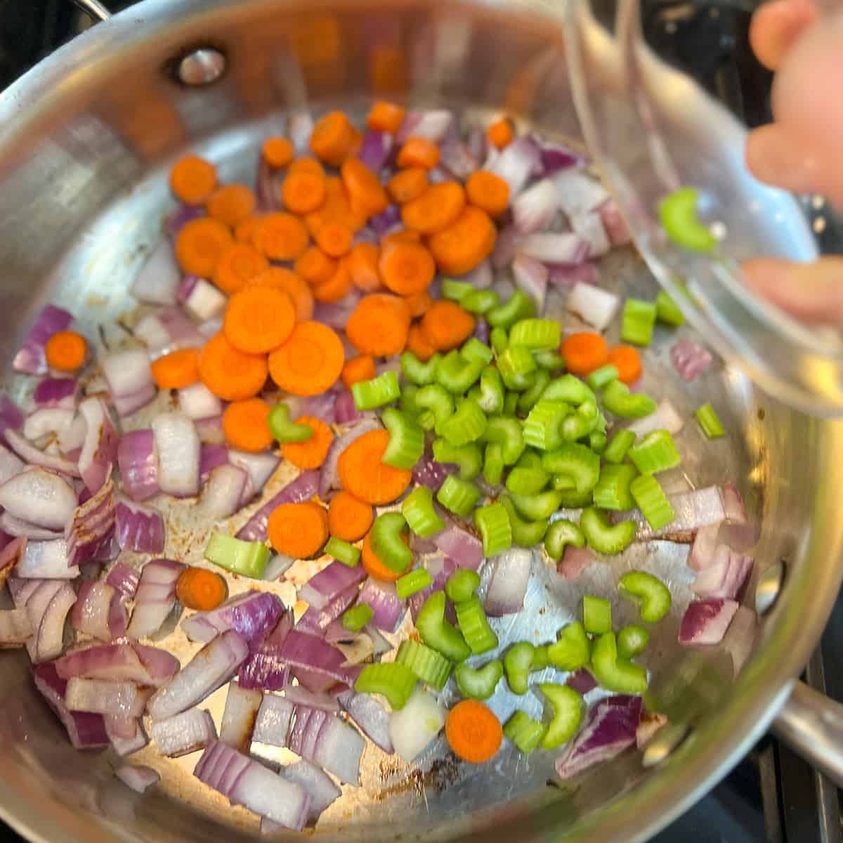 top view of chopped celery being added to sauté pan with chopped onions and carrots.