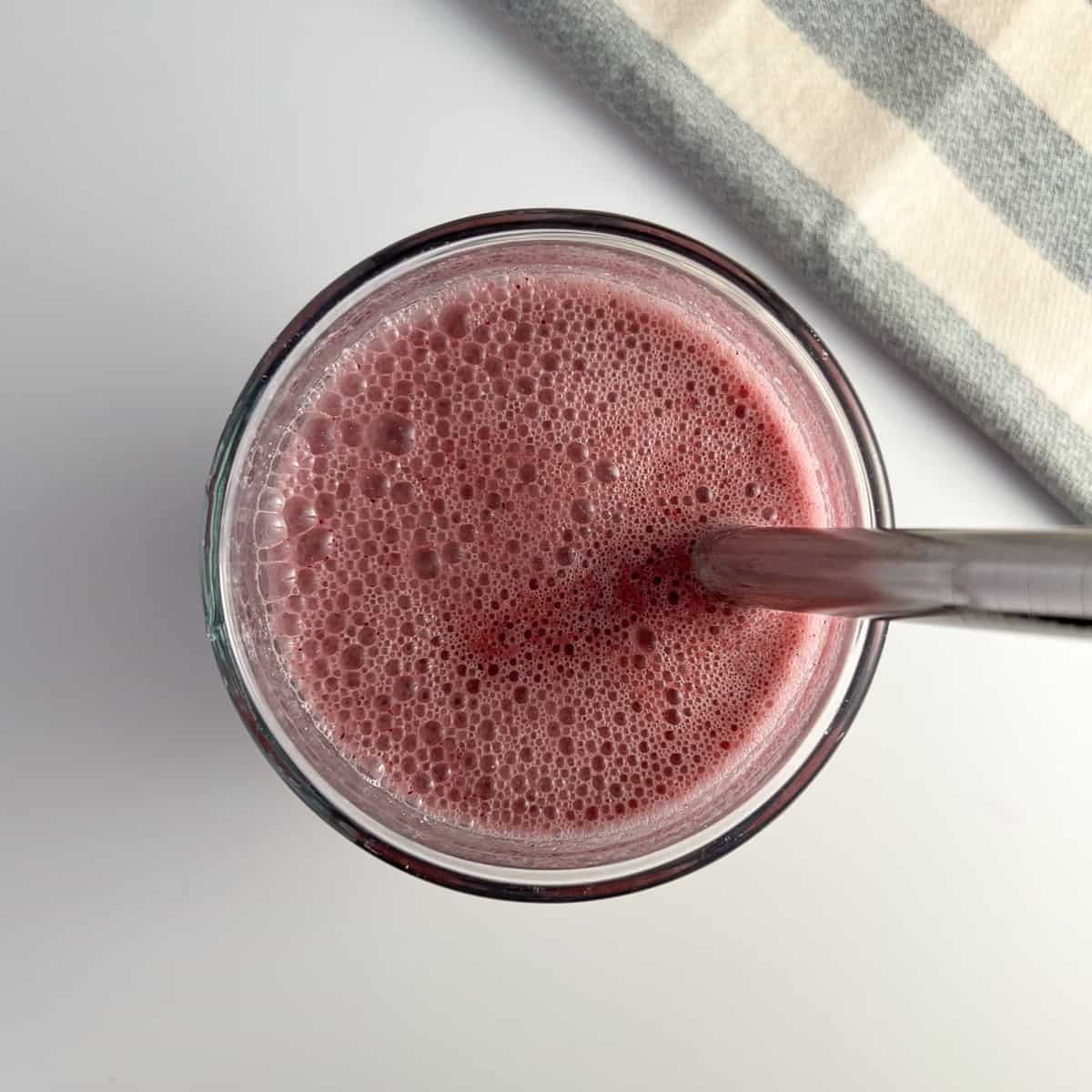 top view close up of pineapple weight loss smoothie in a glass with metal straw; striped blue and white towel on the side