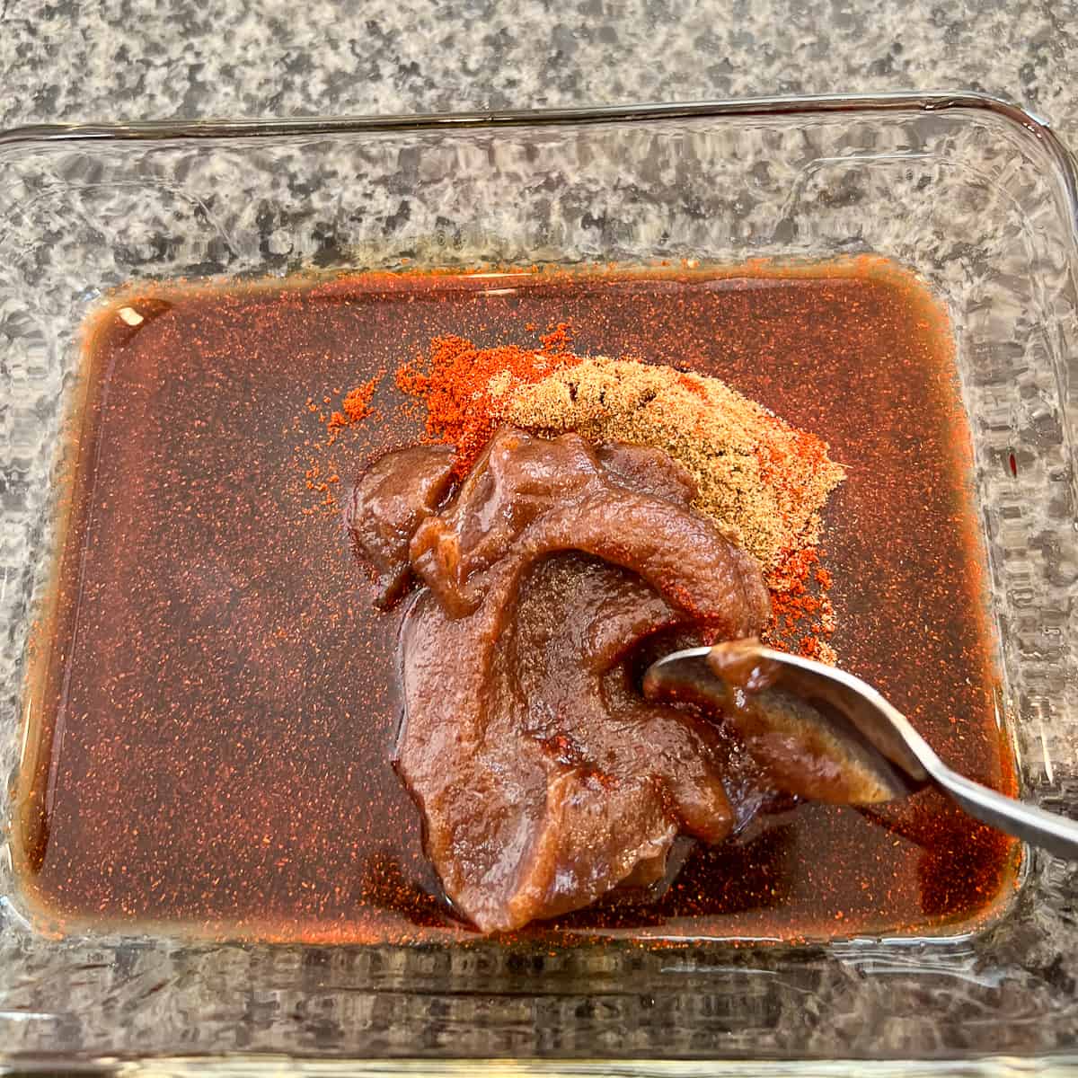 tempeh bacon sauce mixture being combined in a glass dish with a spoon