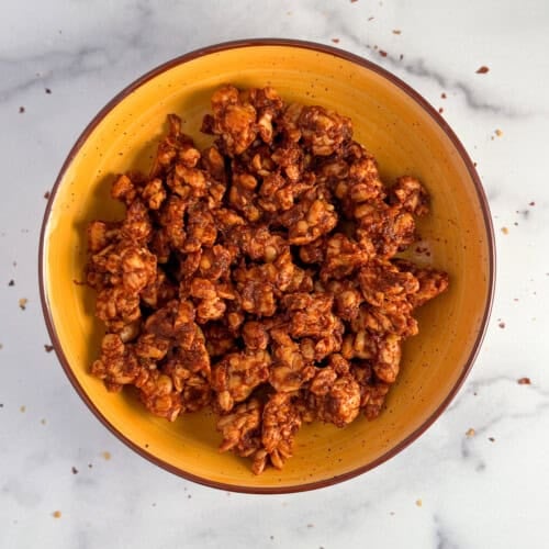 top view close up of tempeh chorizo crumbles in a yellow bowl on white marbled surface