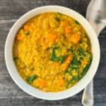 top view of yellow split mung beans with spinach and sweet potato in a white bowl with spoon blurred on the side
