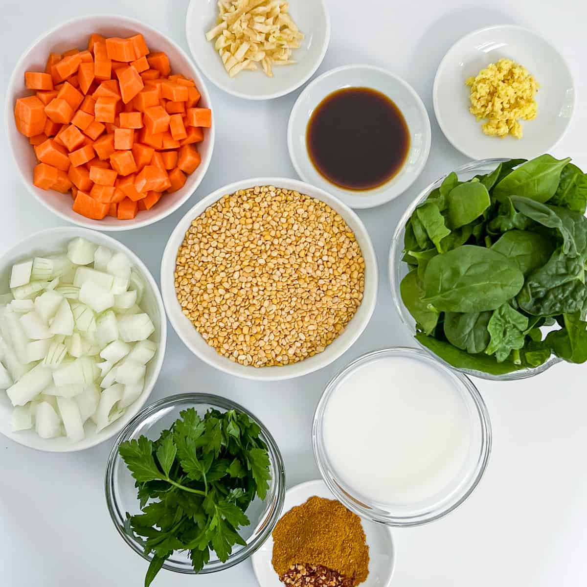 top view key ingredients for split mung beans: yellow split mung beans, diced sweet potato, minced garlic, grated ginger, coconut aminos, fresh spinach, chopped onion, fresh parsley, spices, and coconut milk