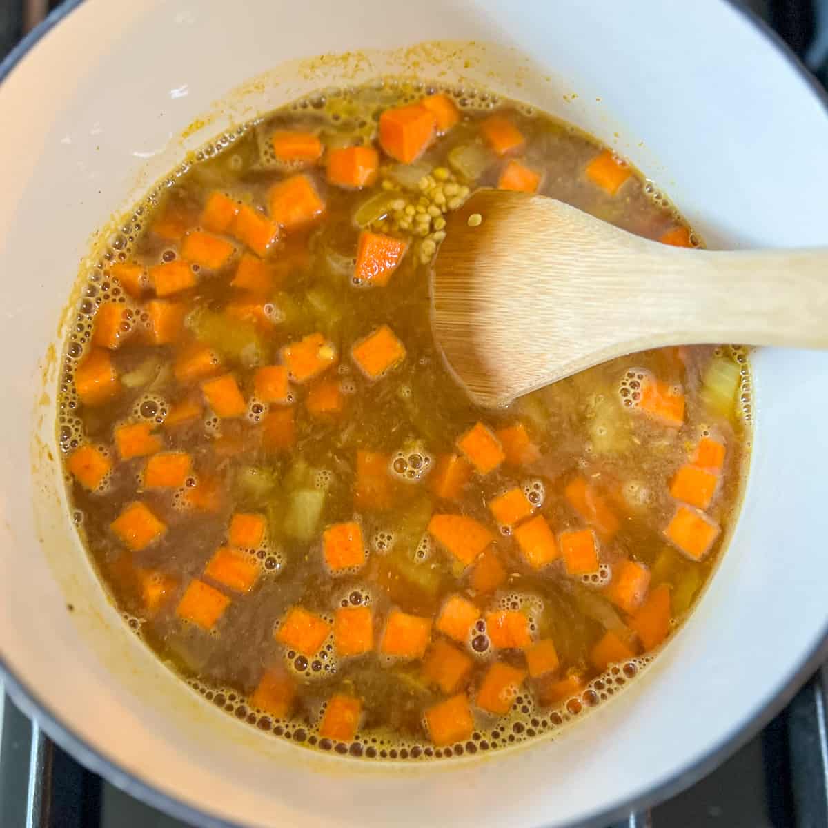 top view of a pot of soup and wooden spoon stirring