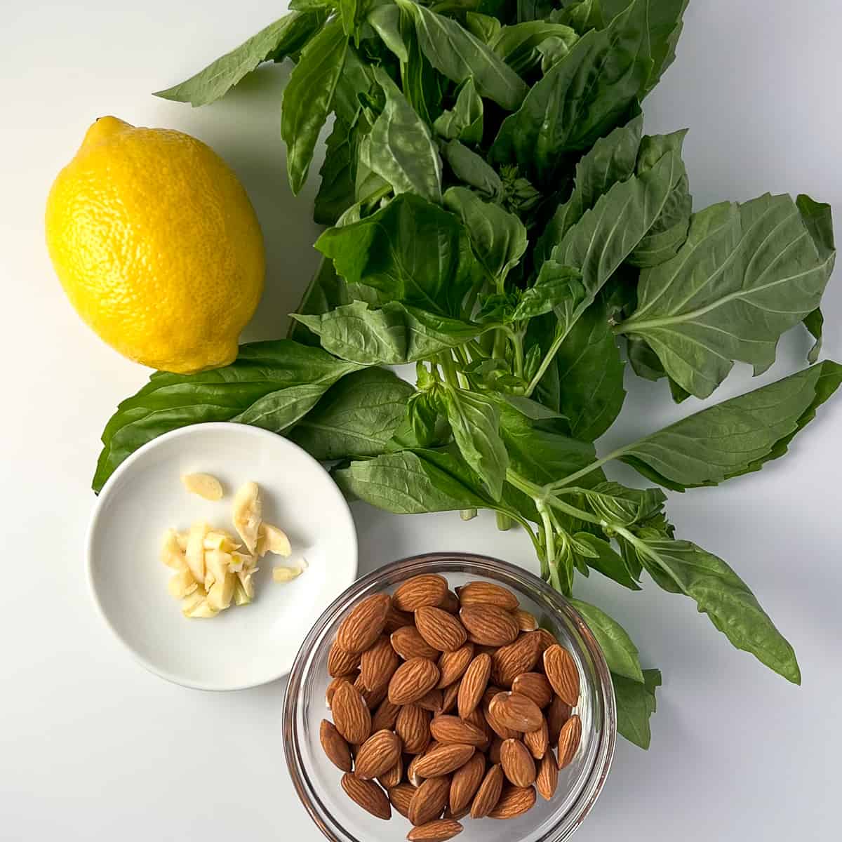 top view of key ingredients for vegan almond pesto: fresh basil, lemon, garlic, almonds