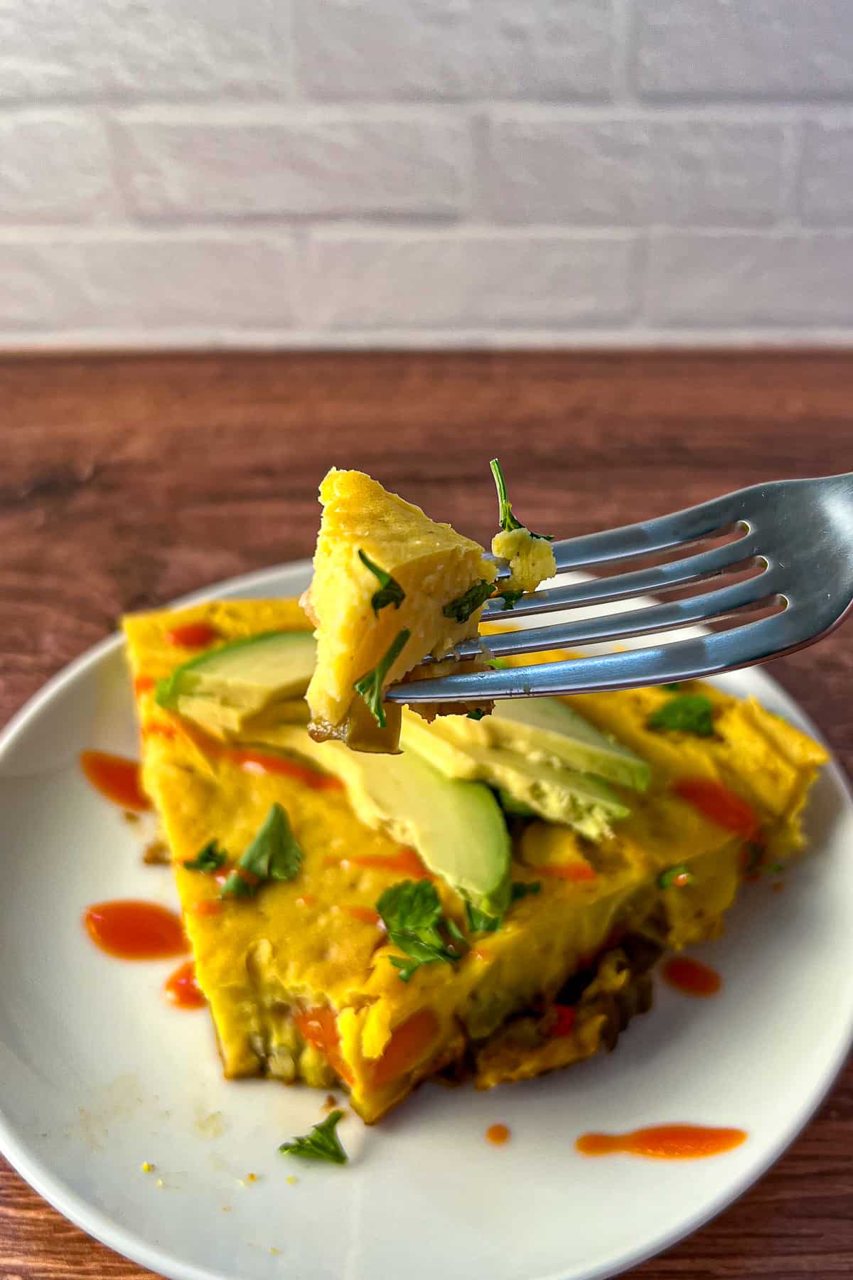 top side view close up of a slice of vegan frittata with a bite size piece on the end of a fork being held up