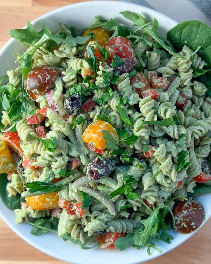 top view close up of vegan pesto pasta salad with tomatoes, red bell pepper, onion, fresh chopped parsley in white bowl