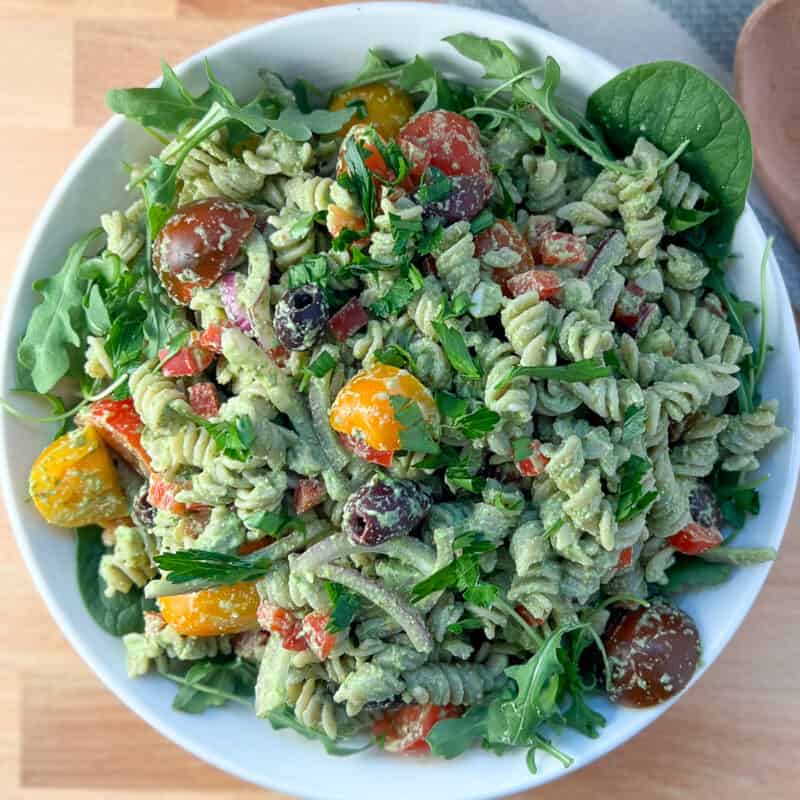 top view close up of vegan pesto pasta salad with tomatoes, red bell pepper, onion, fresh chopped parsley in white bowl