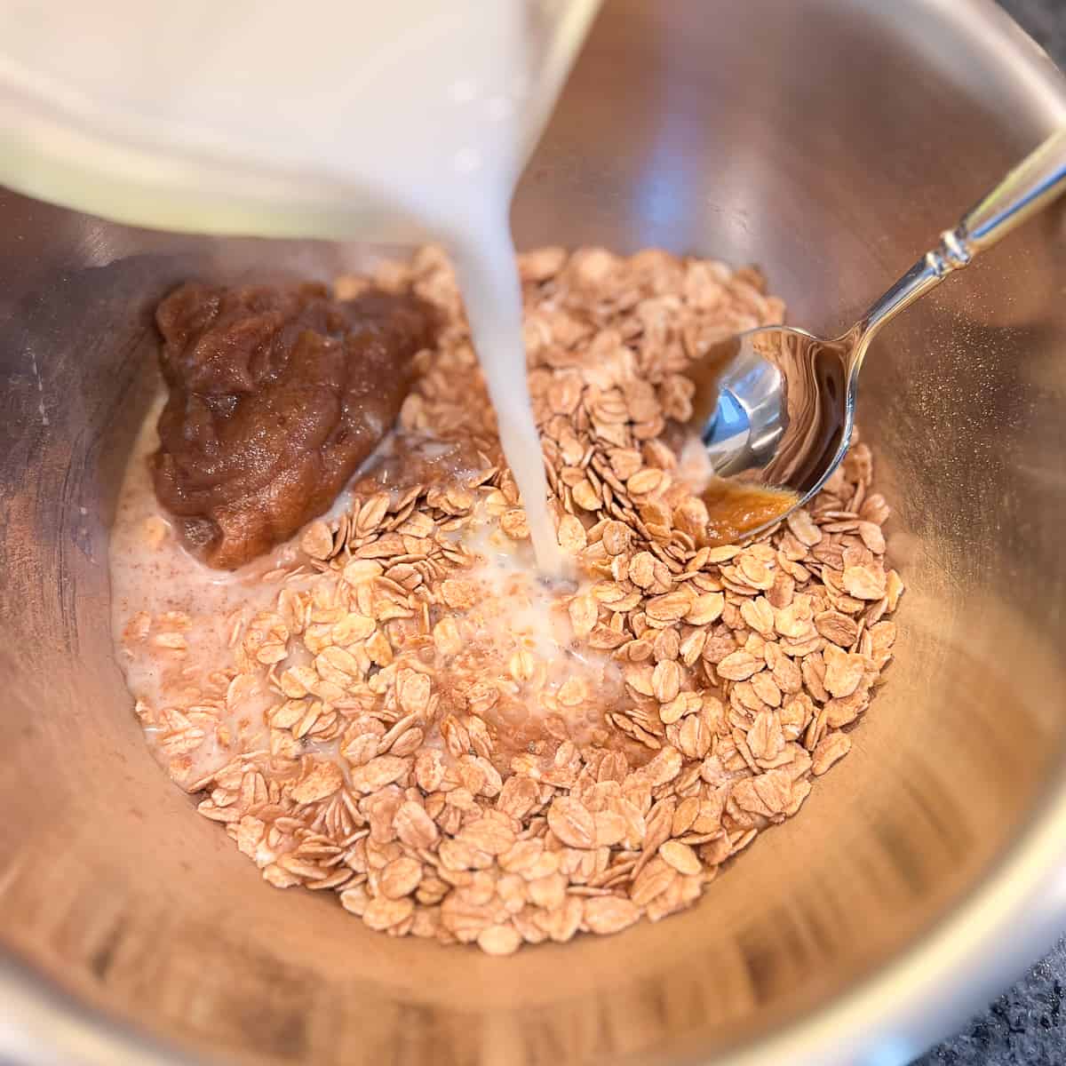 top view of plant based milk being added to a mixing bowl with oats and date syrup