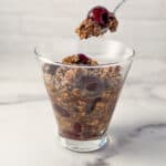 side view close up of black forest overnight oats in a glass dish with a spoon dishing some out