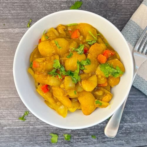 top view of a bowl of curried butter beans topped with fresh chopped cilantro and a fork and striped napkin blurred on the side
