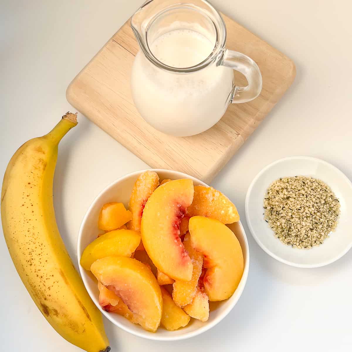 top view of the key ingredients for the peach banana smoothie: almond milk, peaches, banana, hemp hearts