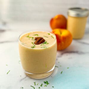 Peach banana smoothie with lime zest and pecans on top; peaches and mason jar blurred in the background.