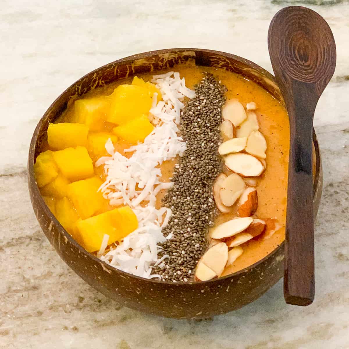 top view close up of energizing tropical fruit smoothie bowl in a wooden bowl with wooden spoon