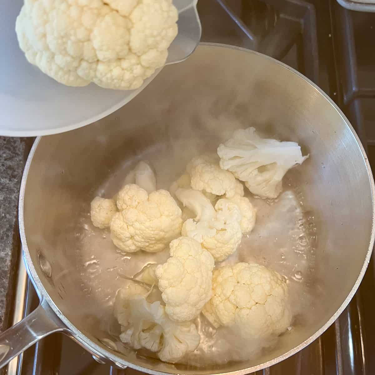 top view of cauliflower florets being added to a pot with boiling water