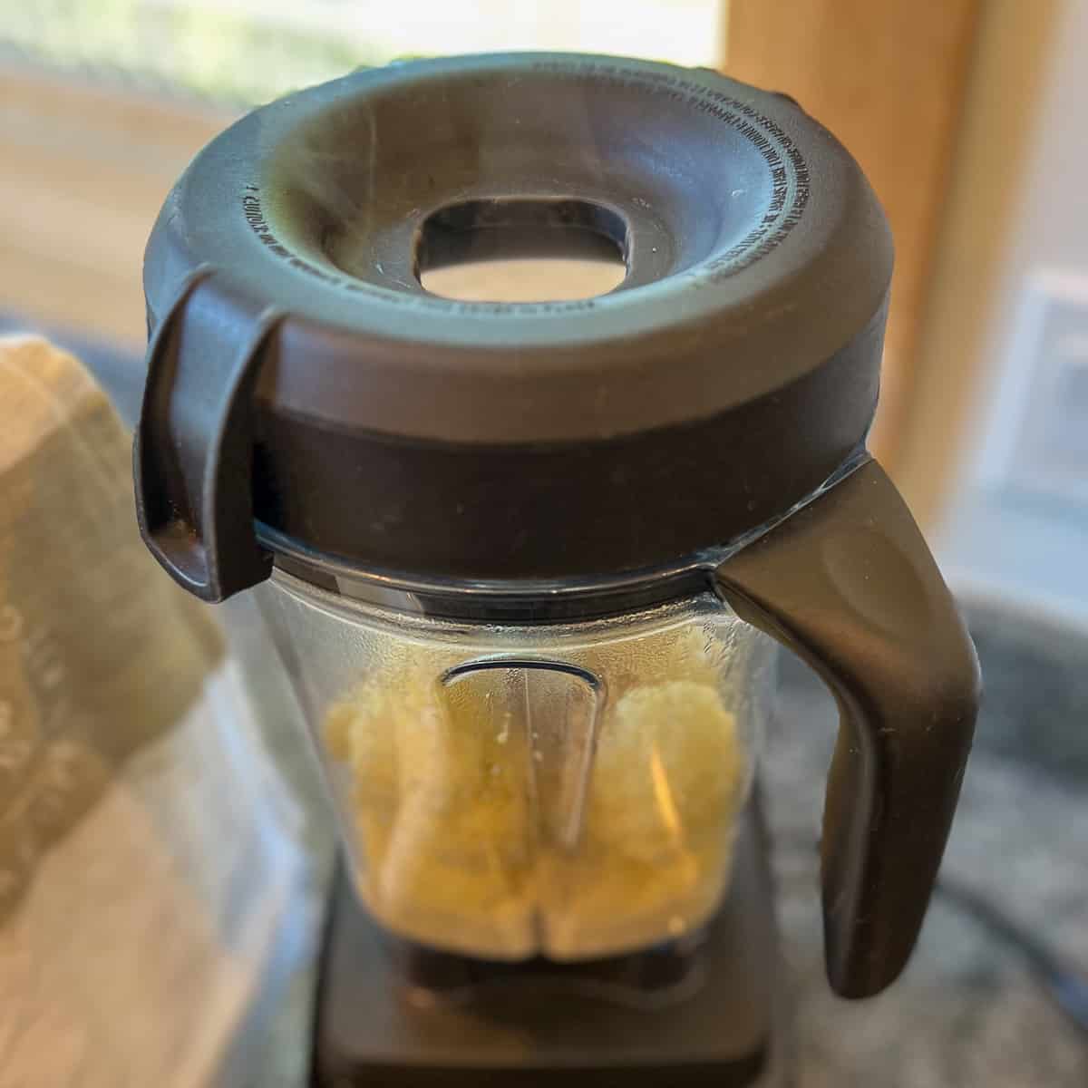 top side view of a blender with hot cauliflower in and steam coming out of the vented lid