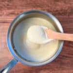 top view of vegan alfredo sauce in a stainless sauce pan with wooden spoon