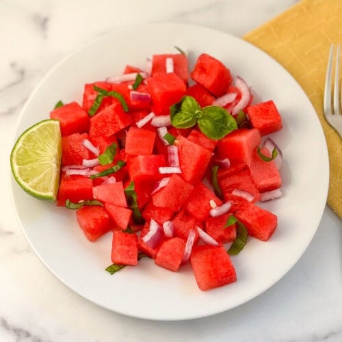 Watermelon basil salad on a plate with a lime wedge on the side.