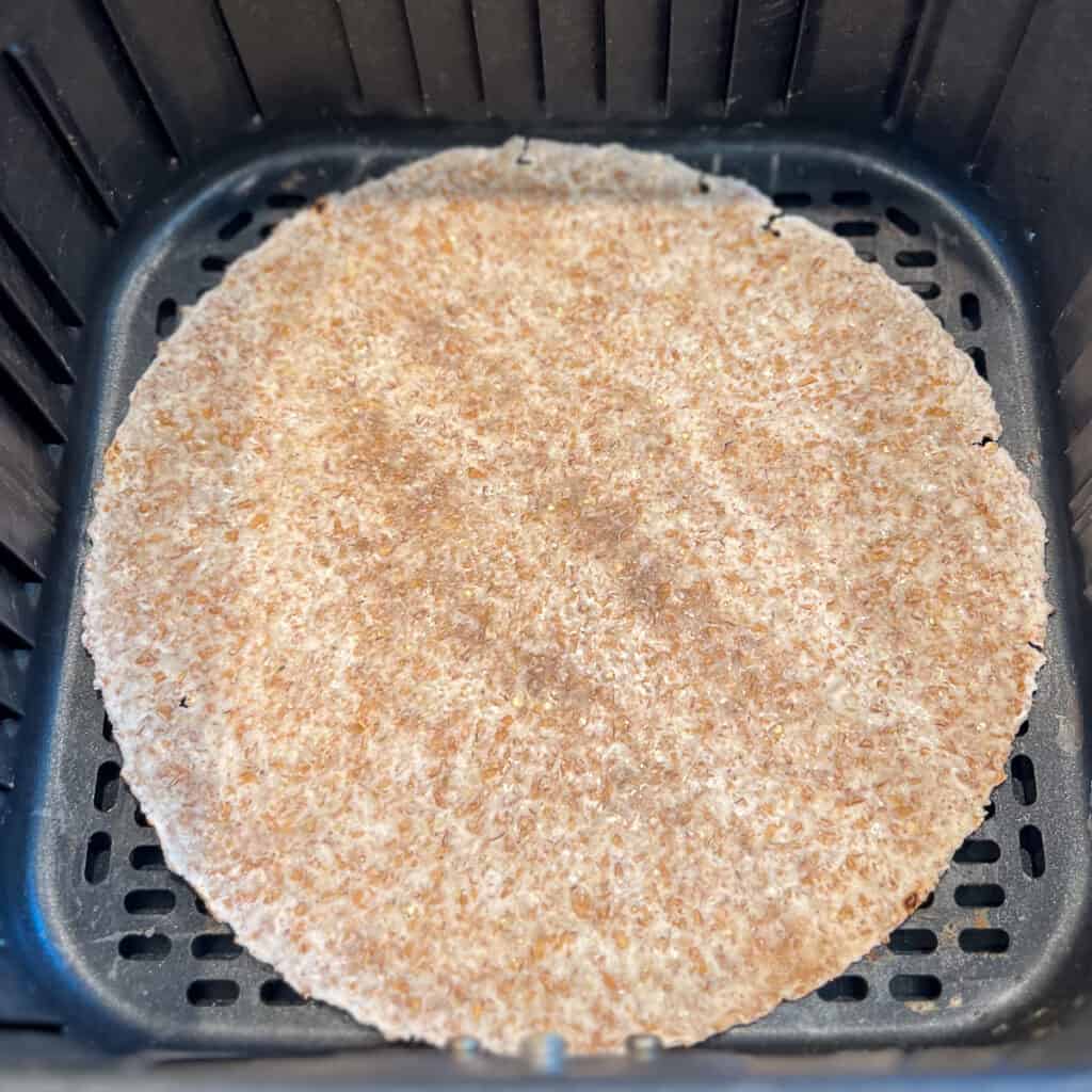 A sprouted grain tortilla in an air fryer basket.
