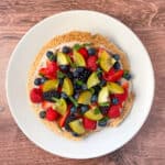 Healthy fruit pizza topped with fresh berries and mint on a plate.