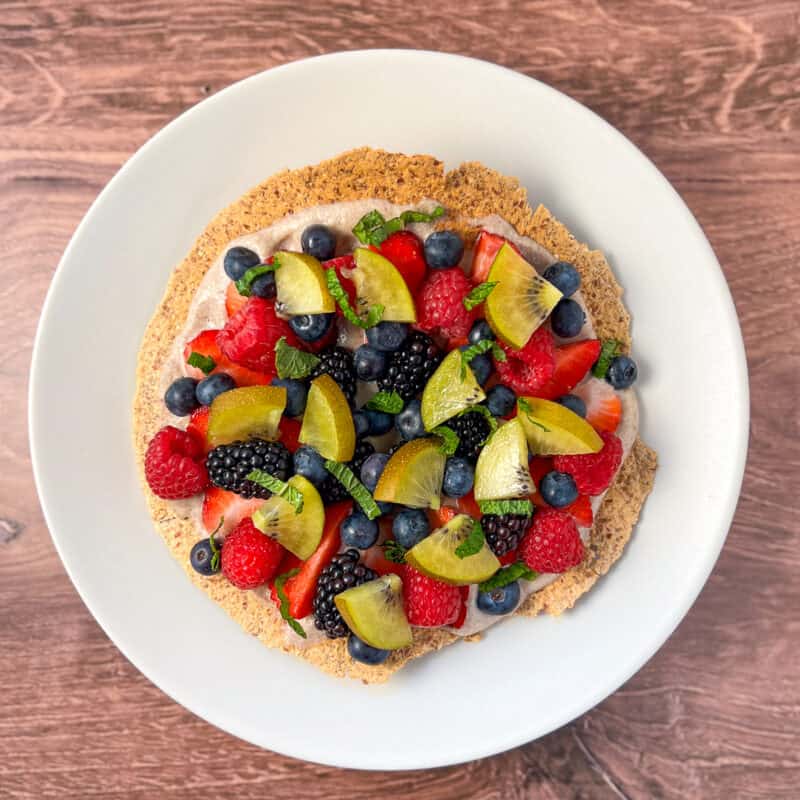 top view of a colorful fruit pizza topped with fresh berries and mint on a white plate